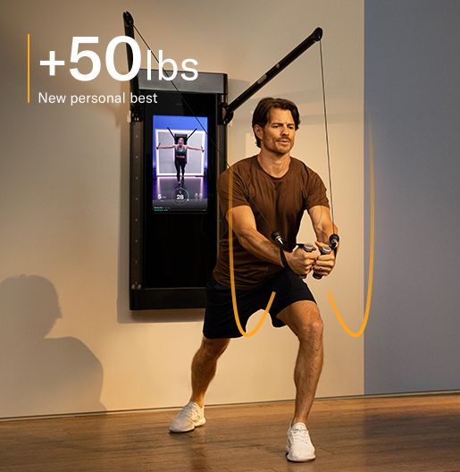 A man is working out in his living room. He is facing away from Tonal, completing a Decline Chest Fly.